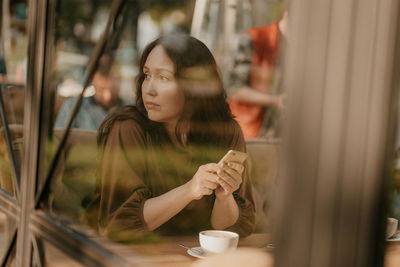 Portrait of young woman drinking coffee from window