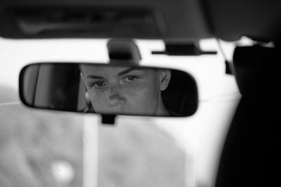 Woman reflecting on rear view mirror of car