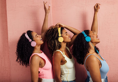 Side view of female friends listening music against wall