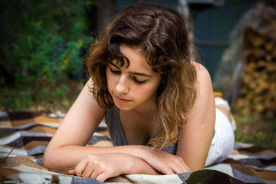 Beautiful teenager girl reading a book lying on blanket on green grass at the forest.
