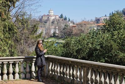 Woman standing at balcony by trees and buildings in town