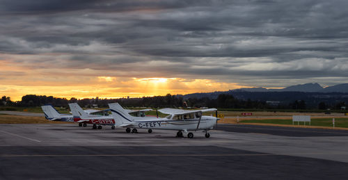 Airplane on runway against sky at sunset