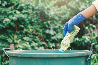 Cropped image of hands throwing plastic bottle in garbage can