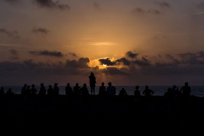 Silhouette people on beach against sky during sunset