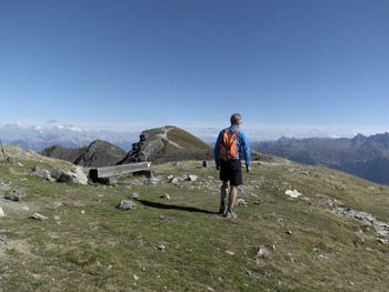 Rear view of man standing on mountain against blue sky