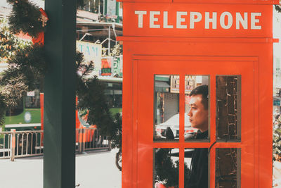 Man standing by red telephone in city