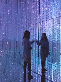 Rear view of people looking at illuminated wall