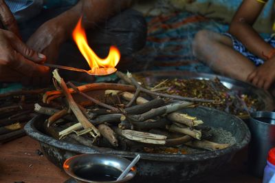 Cropped hand of person holding burning camphor over wooden sticks in container