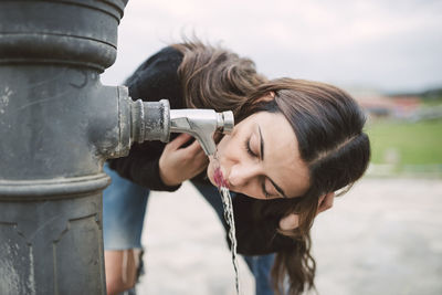 Young woman drinking water from a well