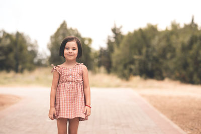 Smiling cute child girl 4-5 year old wearing stylish dress posing in park outdoors closeup.