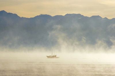 Sailboat amidst mist on sea against sky