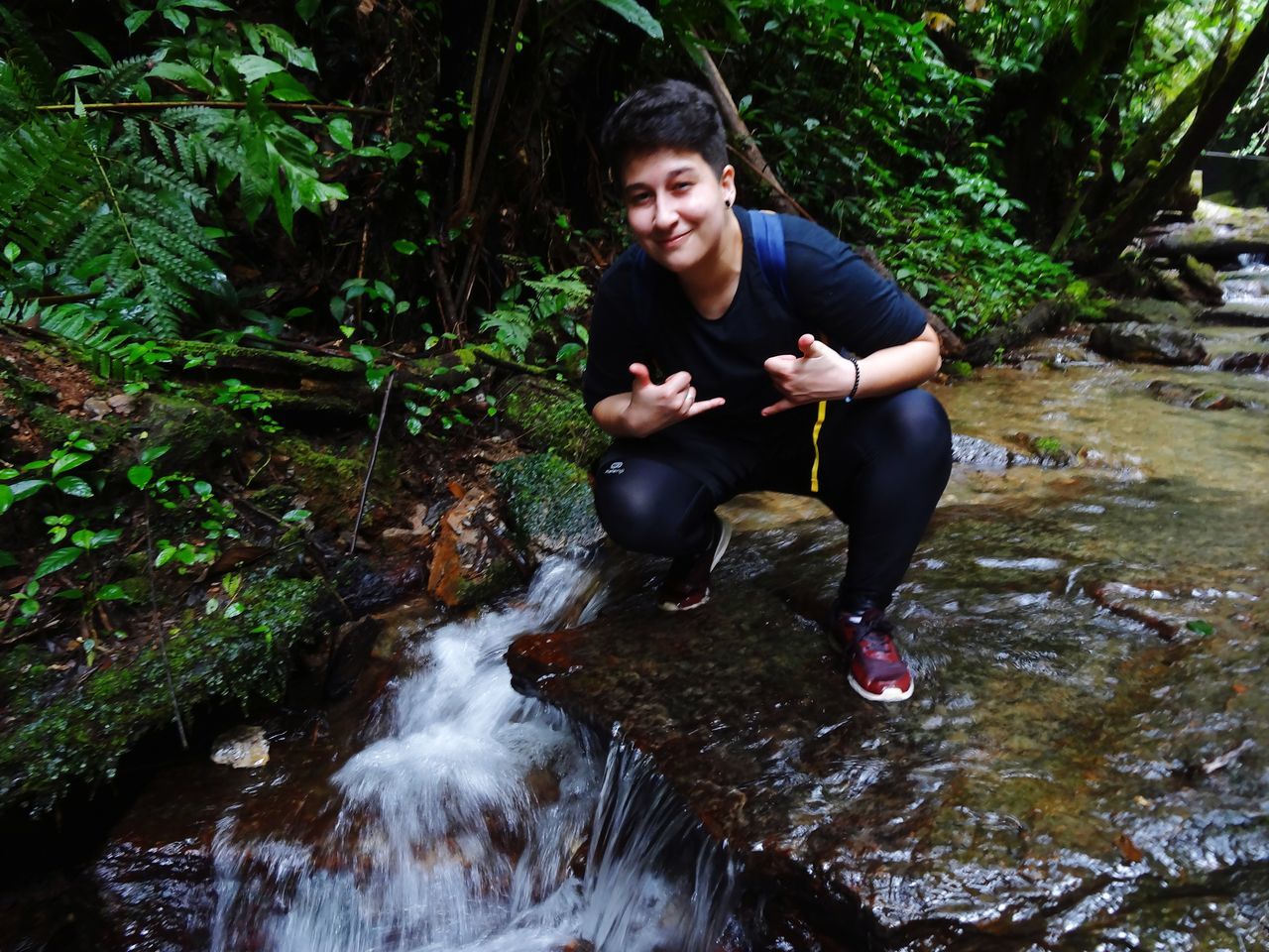 water, one person, nature, stream, tree, forest, plant, waterfall, jungle, river, leisure activity, full length, young adult, adult, wilderness, sitting, lifestyles, rock, motion, land, rainforest, beauty in nature, outdoors, flowing water, environment, day, smiling, men, sports, water feature, activity, casual clothing, front view, portrait, happiness