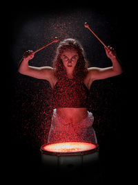 Portrait of young woman playing drum against black background