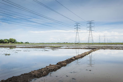 Electricity pylons at farm field against sky