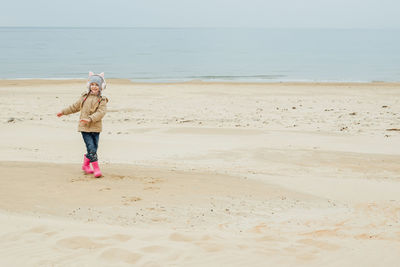 Little girl listens to music in children's pink headphones with cat ears and dances on the beach