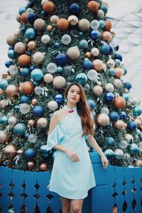 Portrait of smiling young woman standing by christmas tree outdoors