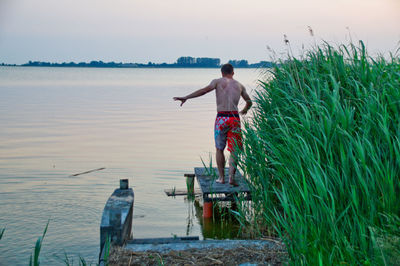 Rear view of man walking on pier against sky during sunset