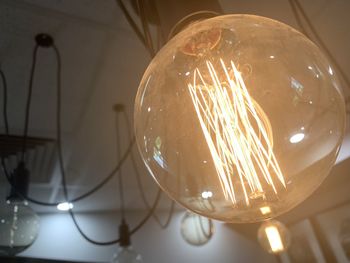 Low angle view of illuminated light bulb hanging from ceiling