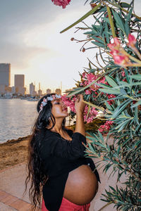 Pregnant woman smelling flowers blooming at lakeshore during sunset