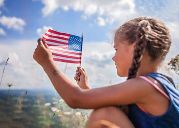 Patriot and national flag day celebration. little patriot sitting on the meadow and holding usa flag