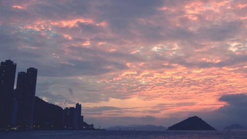 Silhouette buildings by sea against sky during sunset