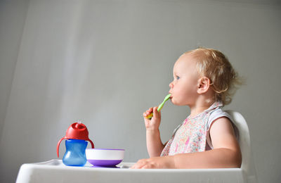 Almost 2 years old baby girl eating rice porridge in her feeding chair. grey background