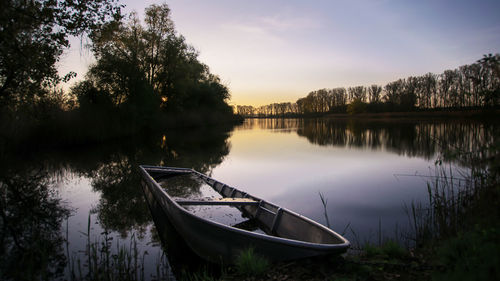 Boat moored in lake against sky during sunset