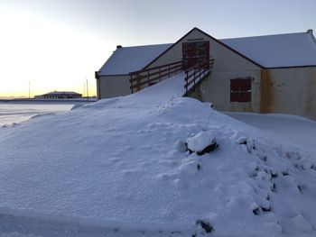 Snow covered houses on field by buildings against sky