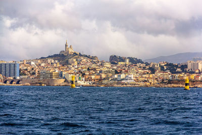 View of buildings by sea against cloudy sky