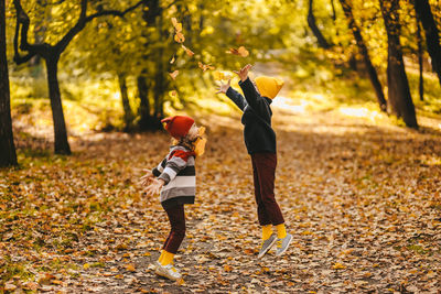 Happy cheerful children in warm clothes have fun walking running in autumn park playing with leaves