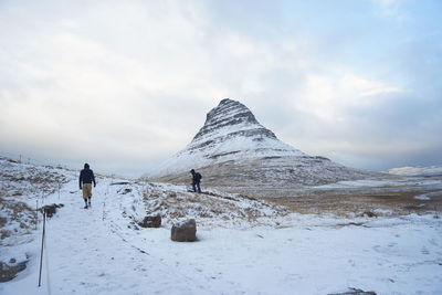 People climbing on snowcapped mountain against sky