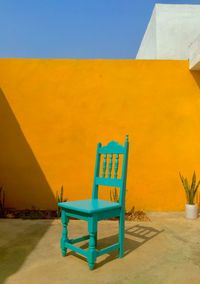 Empty chair against yellow wall and building against sky