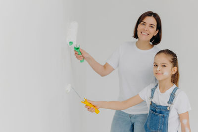 Portrait of smiling mother and daughter painting wall at home