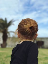 Side view of girl with hair bun against sky