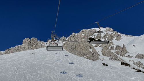 Ski lift over snowcapped mountains against clear blue sky
