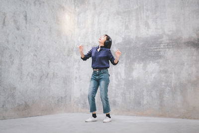 Full length of woman listening music while standing against wall