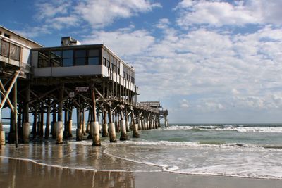 Low angle view of pier over beach against cloudy sky