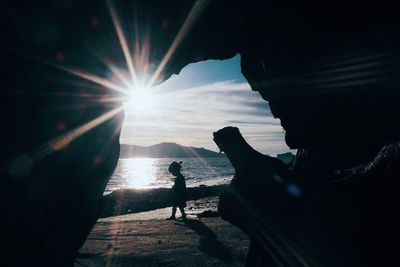 Silhouette man by sea against bright sun