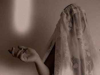 Thoughtful woman covered with fabric gesturing while standing against wall