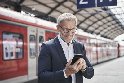 Male professional using mobile phone while standing on railroad platform