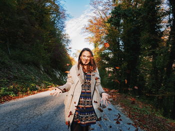 Portrait of smiling young woman on road amidst trees