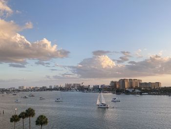 Sailboats in sea by buildings against sky during sunset