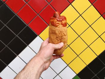 Cropped hand holding bread roll in front of tiled wall