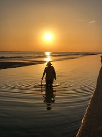 Rear view of silhouette man standing in sea against sky during sunset