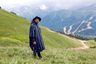 Man with a beard shepherd standing in the mountains in a black raincoat in the rain