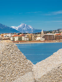 Buildings by sea against blue sky