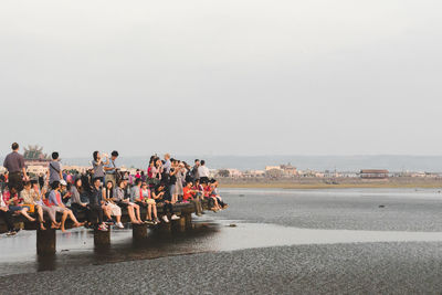 People on pier over sea against clear sky during sunset