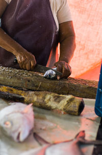 Midsection of woman cutting fish on wood in market