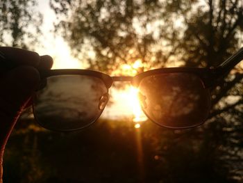 Close-up of hand holding sunglasses against sunset sky