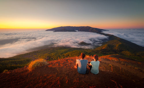 Rear view of people looking at mountains against sky during sunset